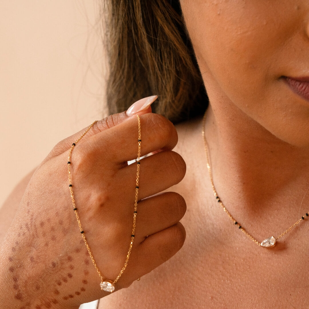 Woman wearing a Modern Mangal mangalsutra and holding another, showcasing the delicate gold chain with black beads and a sparkling pendant.