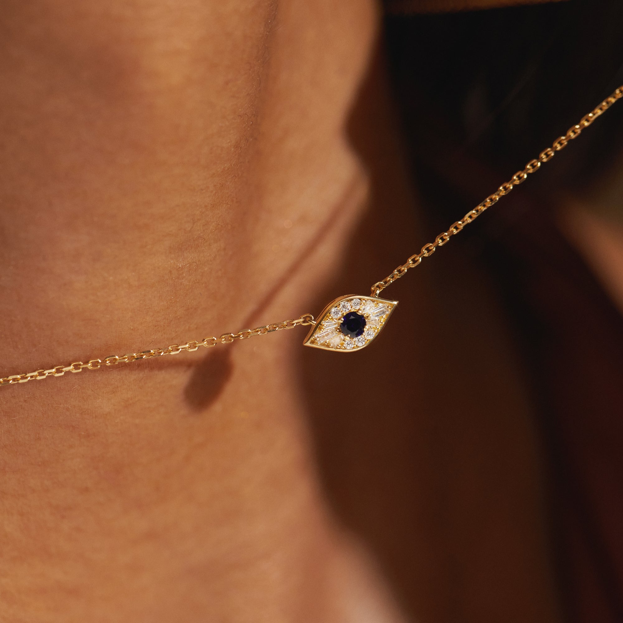 Close-up of the Modern Mangal Amina Necklace evil eye pendant showcasing a luminous round-cut sapphire surrounded by precision-set baguette and round diamonds in 18K yellow gold bezel detailing.