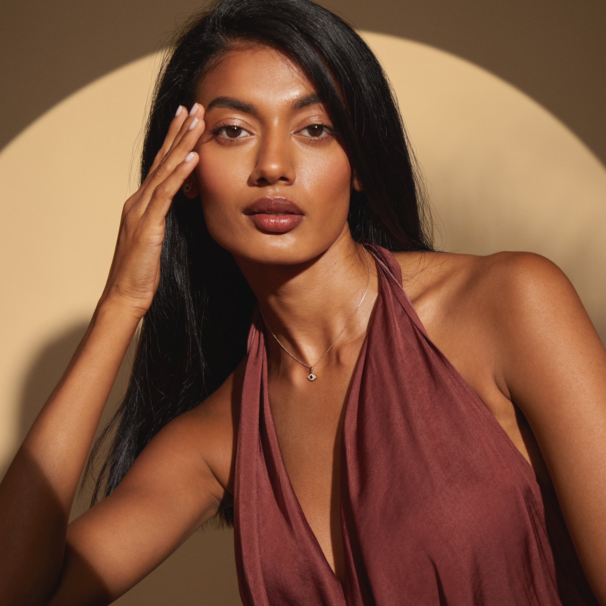 Model styled in deep rust dress showcasing the Modern Mangal Amina Necklace in full frame, with delicate chain and sapphire-studded evil eye pendant exuding subtle elegance and symbolic protection.
