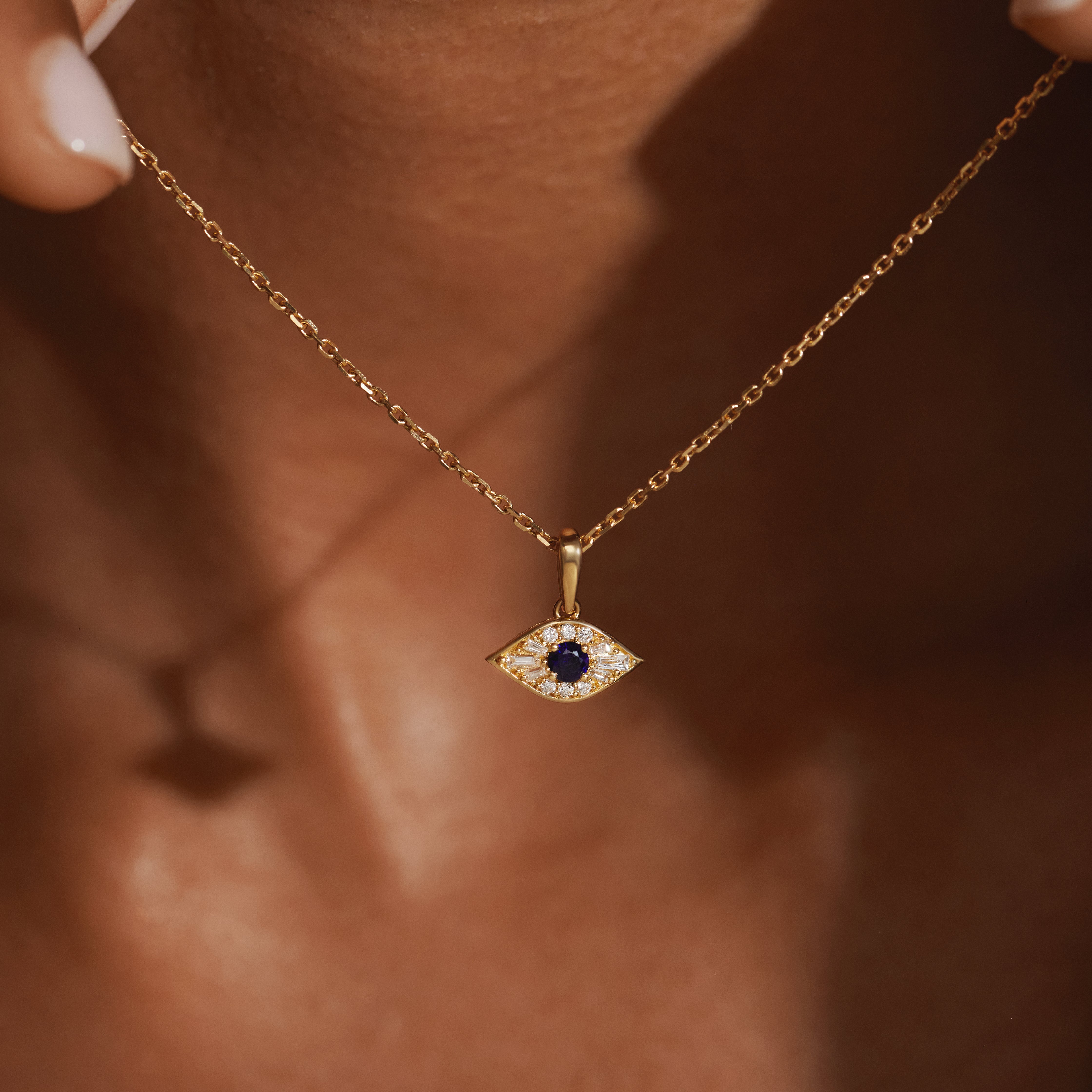 Macro shot of the Modern Mangal Amina Necklace pendant with sapphire center framed by baguette and round-cut diamonds, held in a smooth bezel setting crafted in 18K yellow gold.