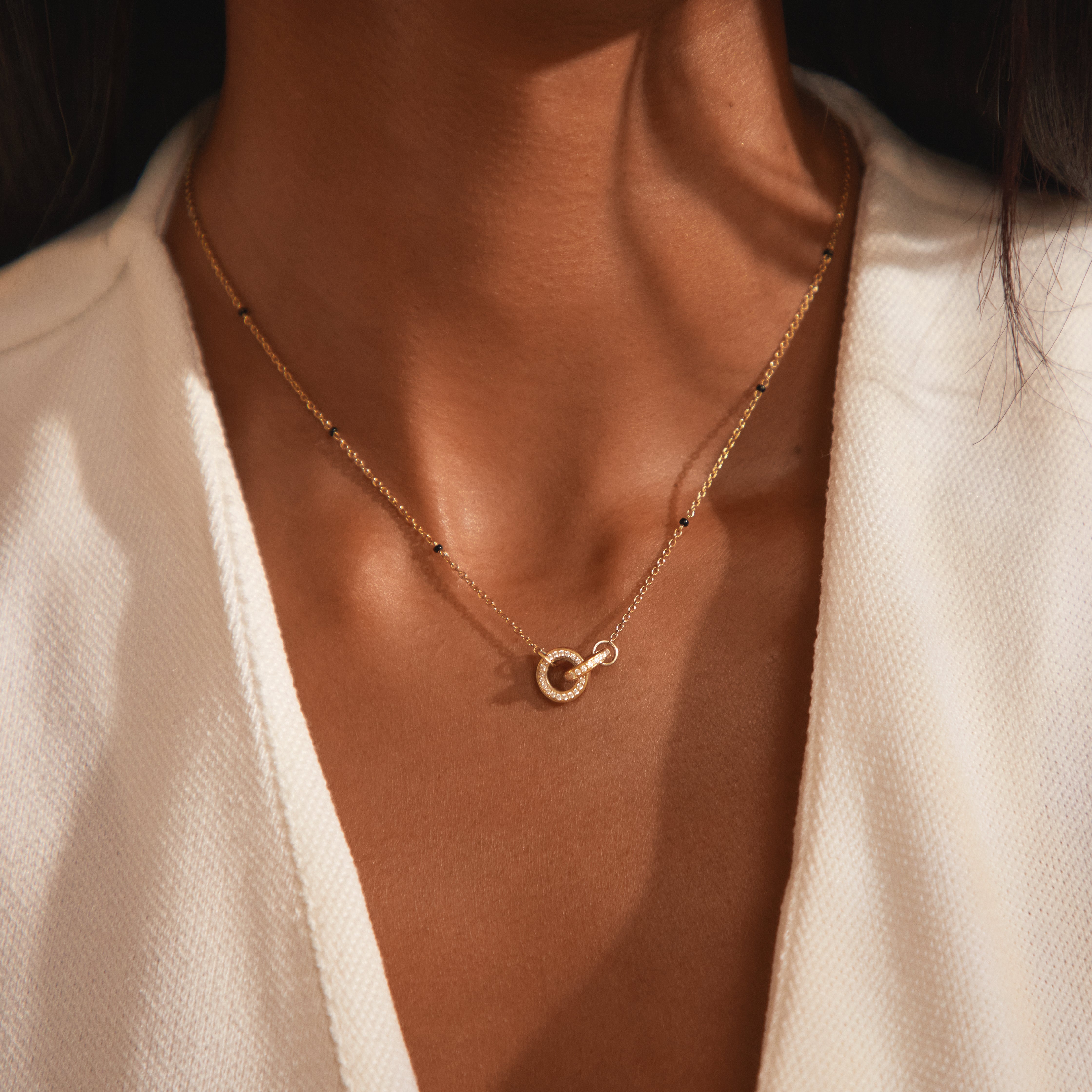 Close-up of Modern Mangal's Anvita Mangalsutra worn in 18K yellow gold — two interlocking lab-grown diamond circles resting against the skin, with black glass beads along the chain.