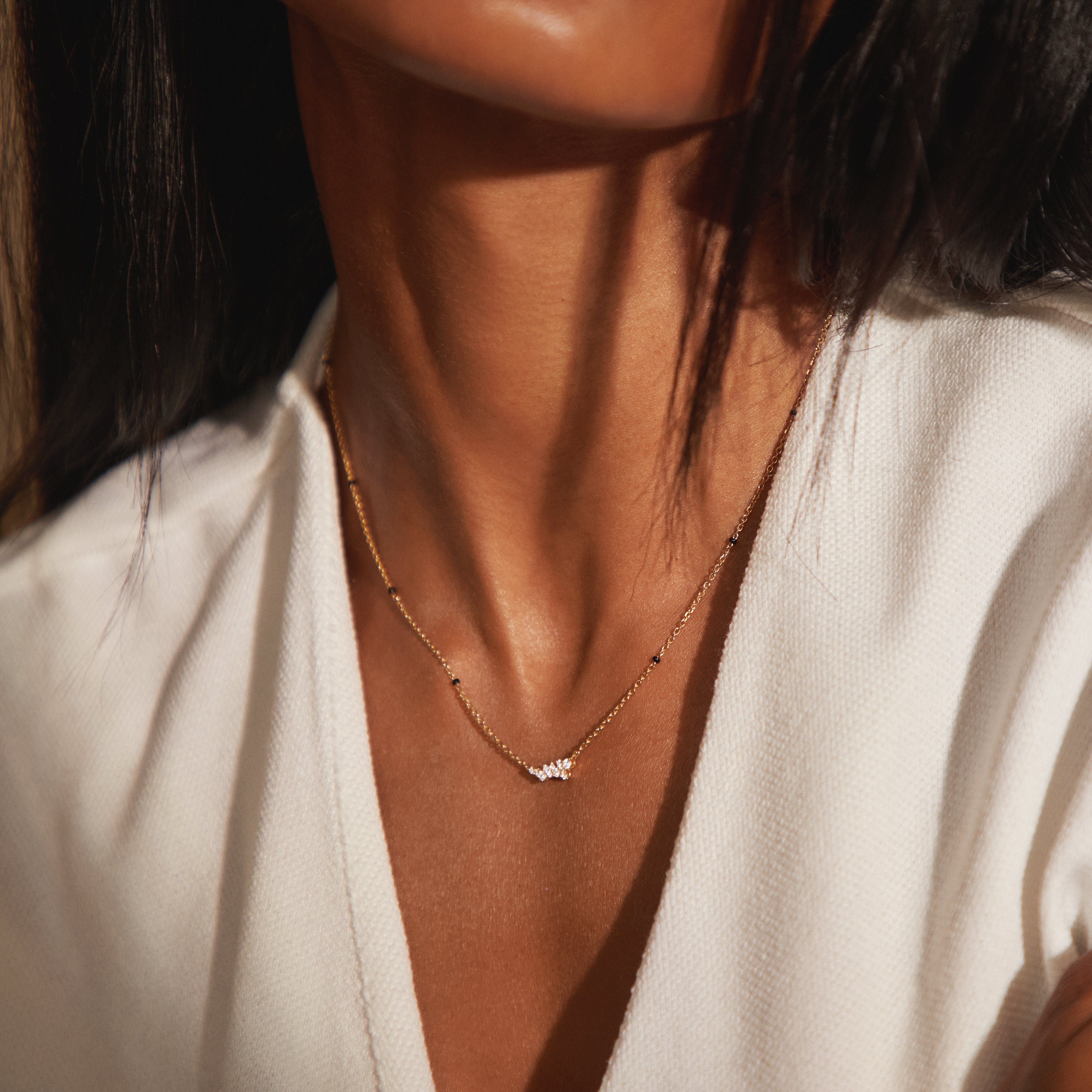 Close-up of Modern Mangal's Nakshi Mangalsutra worn in 18K yellow gold — the eleven-diamond constellation cluster resting against the skin, with black glass beads along the Peace Chain.