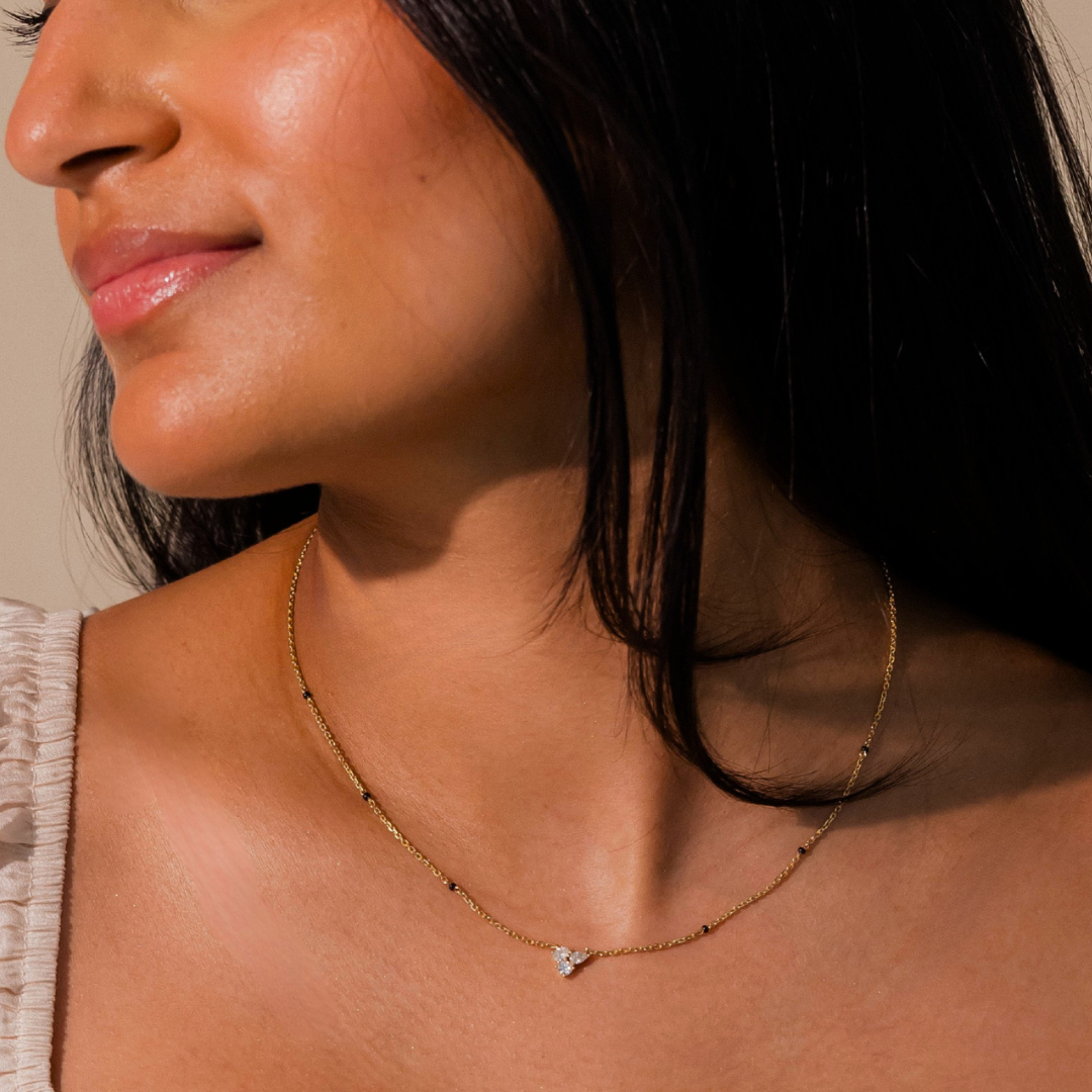 Close-up of Modern Mangal's Reema Mangalsutra worn in 18K yellow gold — a cluster of round, pear, and oval lab-grown diamonds resting against the skin on a Peace Chain with four black glass beads.