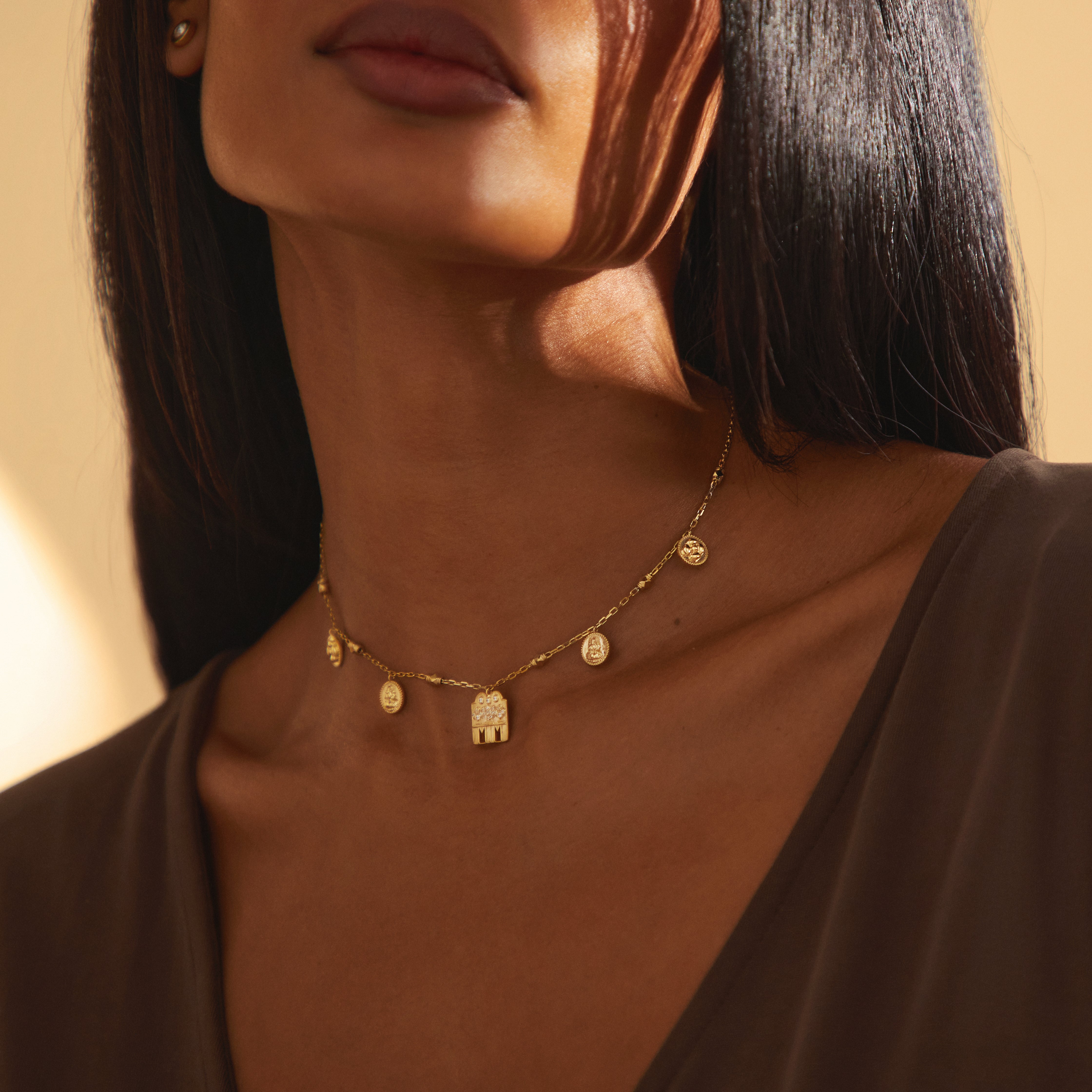 Close-up of the Sravya Mangalayam necklace in yellow gold from Modern Mangal, showing the intricate diamond-set Shivling pendant and flanking Lakshmi and floral kasu charms on the chain.