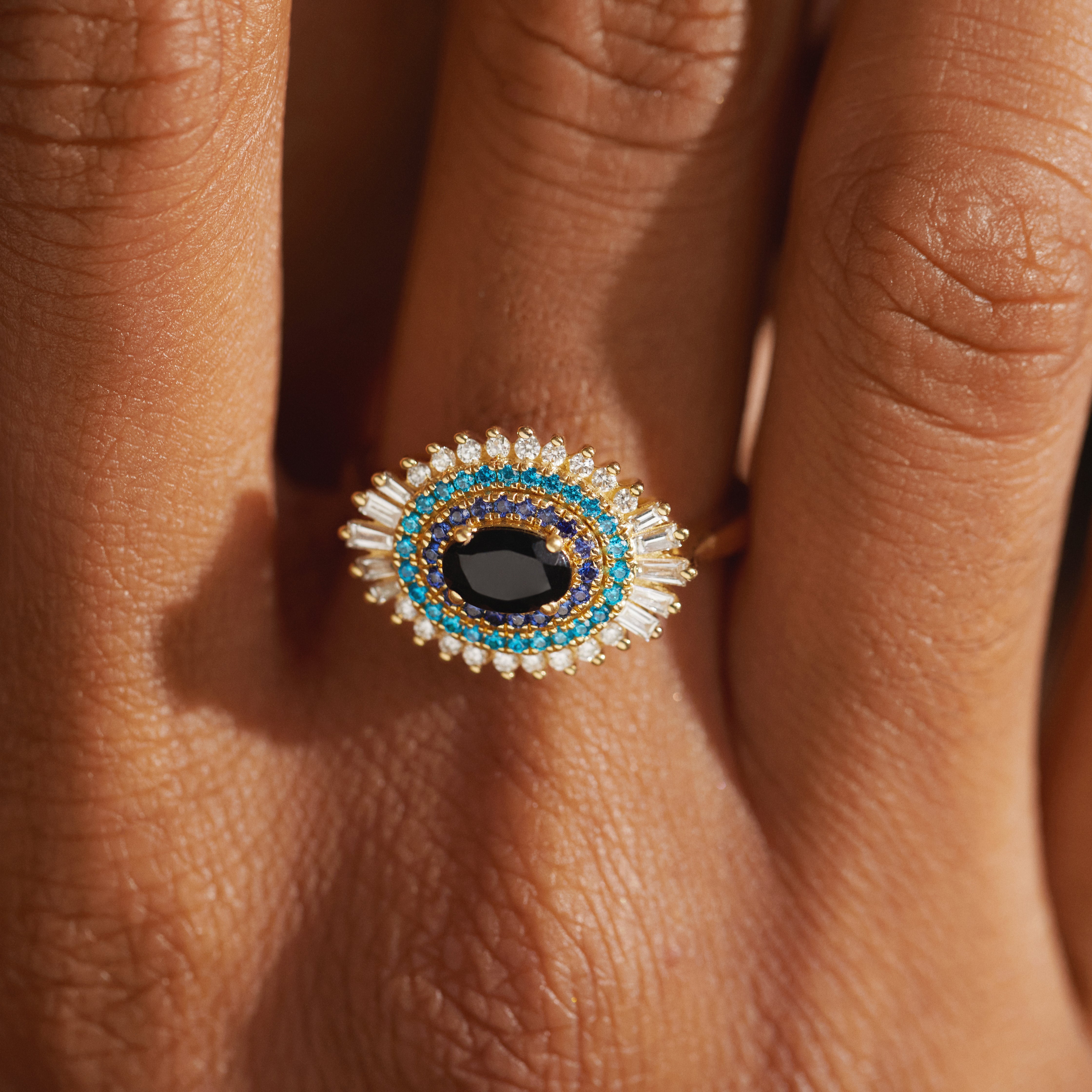 Close-up of the Modern Mangal Safiya Ring in 18K yellow gold with black onyx center, surrounded by bright turquoise blue sapphires and baguette diamonds, worn on a model’s hand.