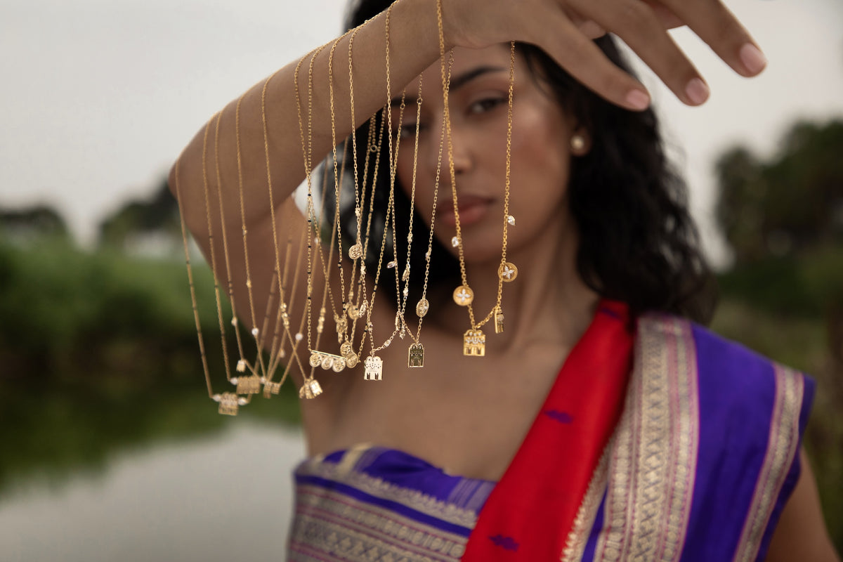 Gold thaali pendants on fine chains, held up in front of a silk sari
