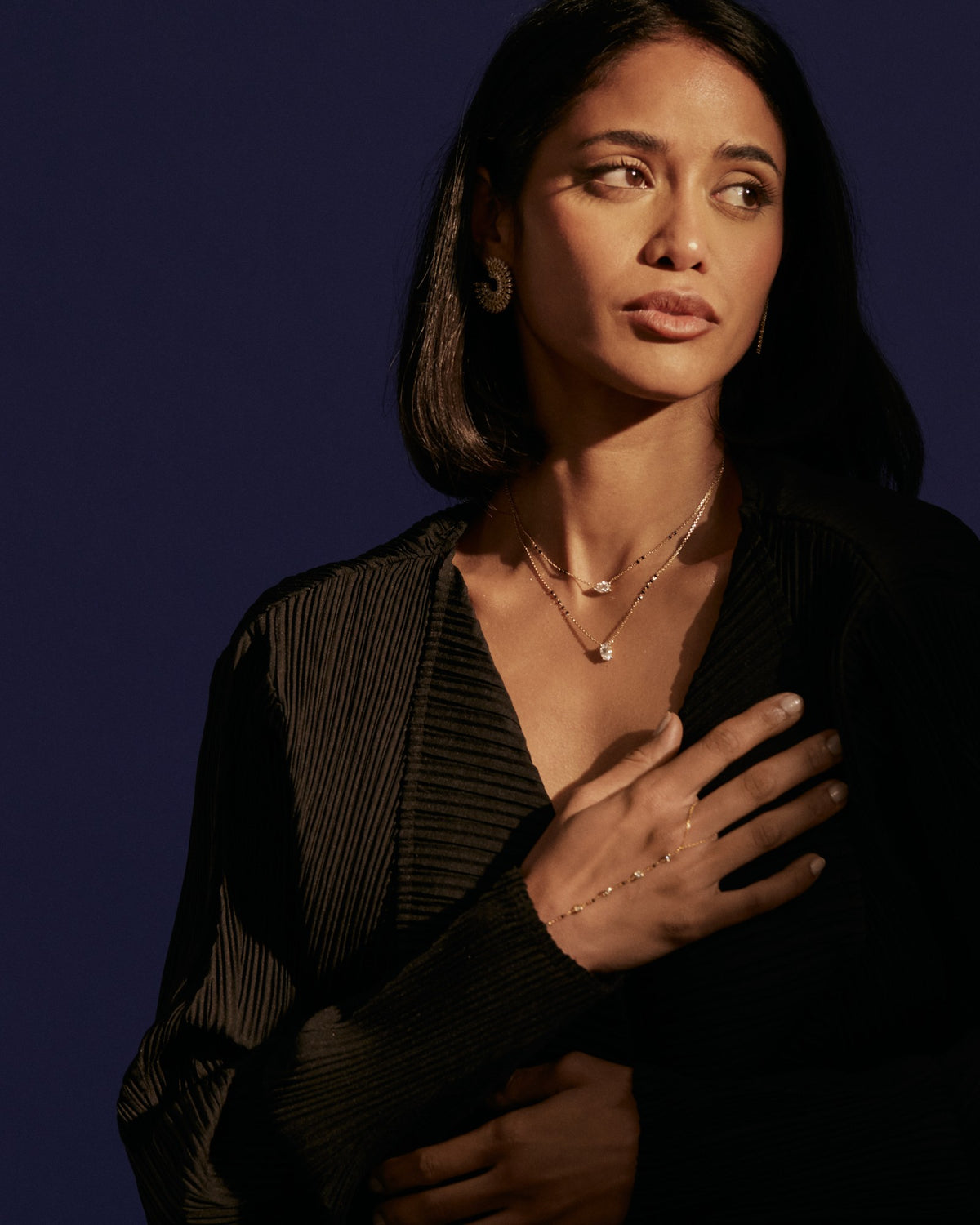 A model in a black wrap top wearing layered diamond mangalsutras in 18K gold, against a deep navy backdrop