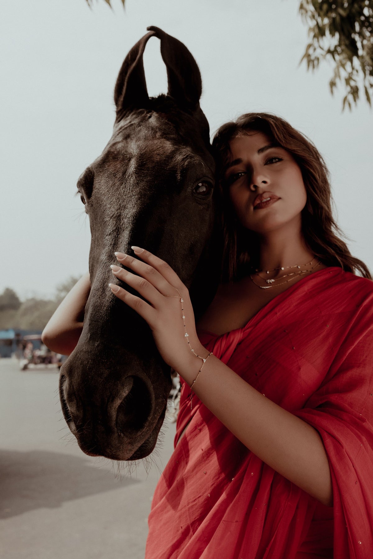 A woman in a red saree resting her hand on a horse in Jaipur