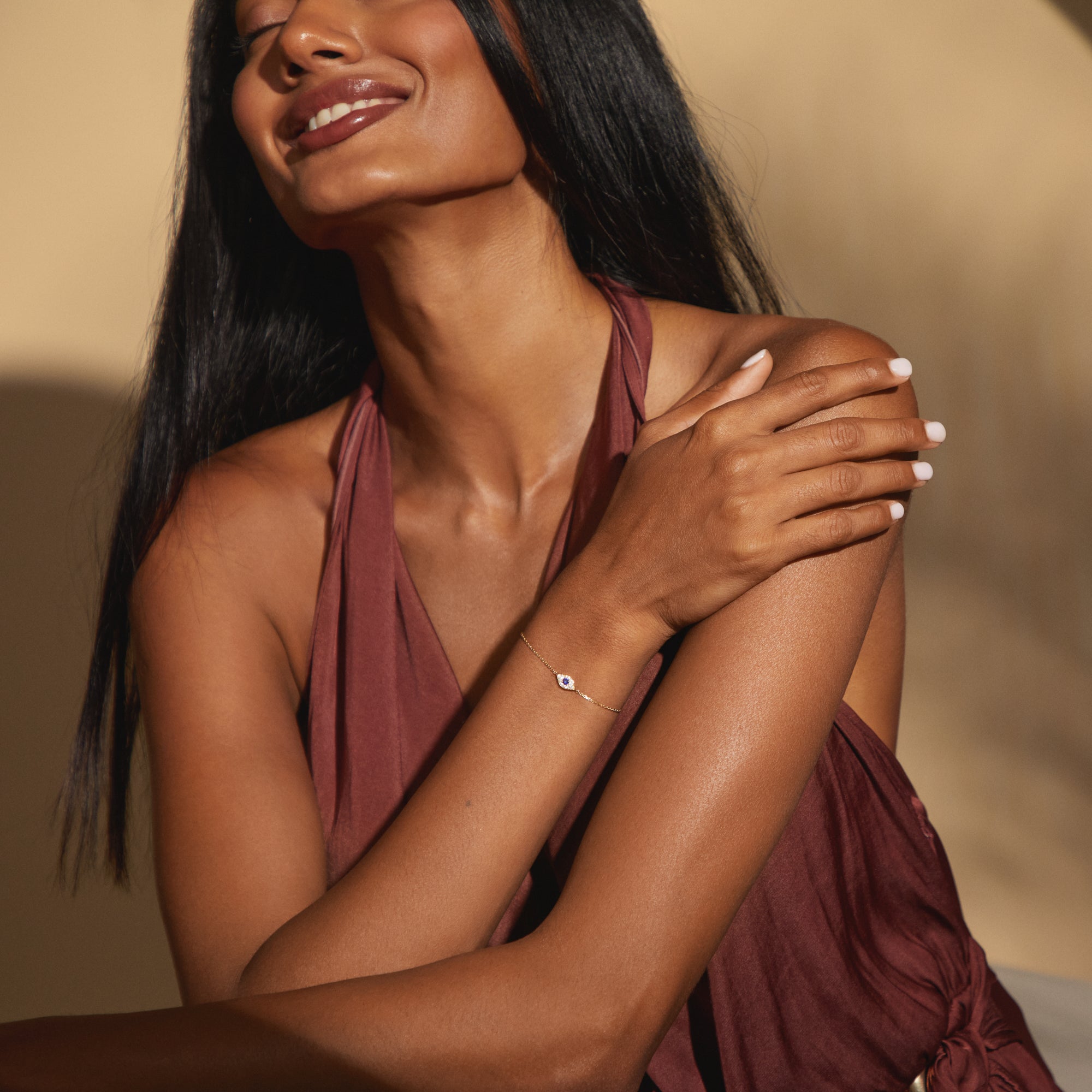 Model smiling while wearing the Aira Bracelet by Modern Mangal, capturing its delicate gold chain and symbolic sapphire evil eye detail in a natural lifestyle setting.