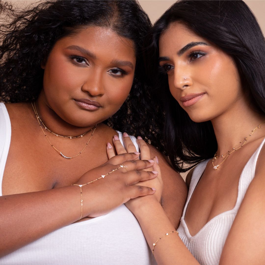 Two models wearing jewelry from the Modern Mangal x Ashna Gray Ashna Collection, including layered necklaces and bracelets that honor South Asian heritage with a modern twist. The collection celebrates strength, elegance, and individuality.