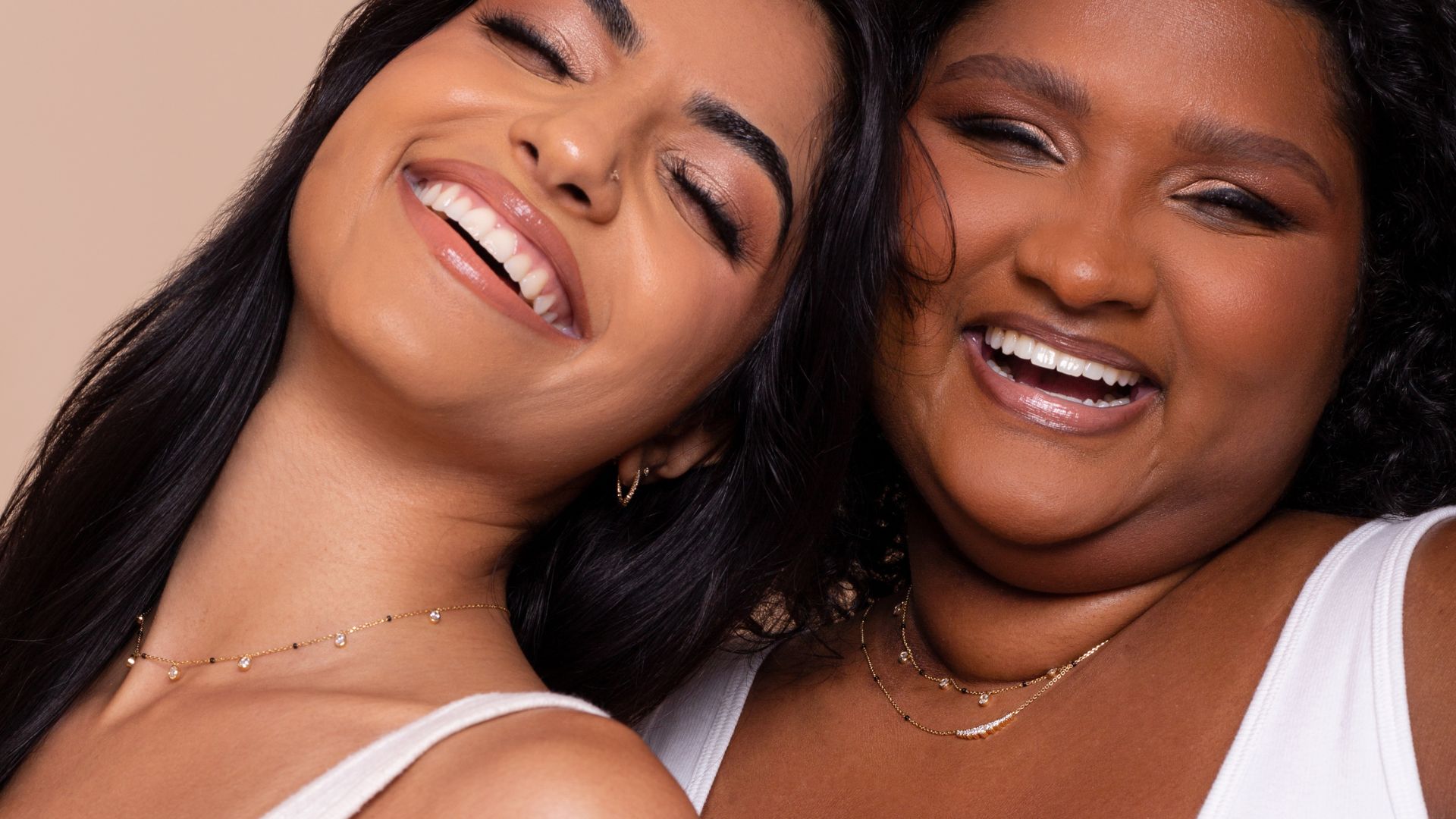 Two models smiling and wearing jewelry from the Modern Mangal x Ashna Gray Collection, showcasing delicate layered necklaces that blend traditional elegance with a modern style, embodying joy, strength, and individuality.