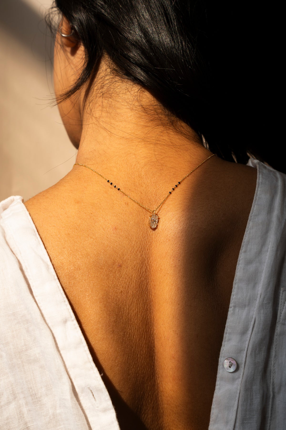 Hands fastening the clasp of a fine gold mangalsutra at the back of the neck