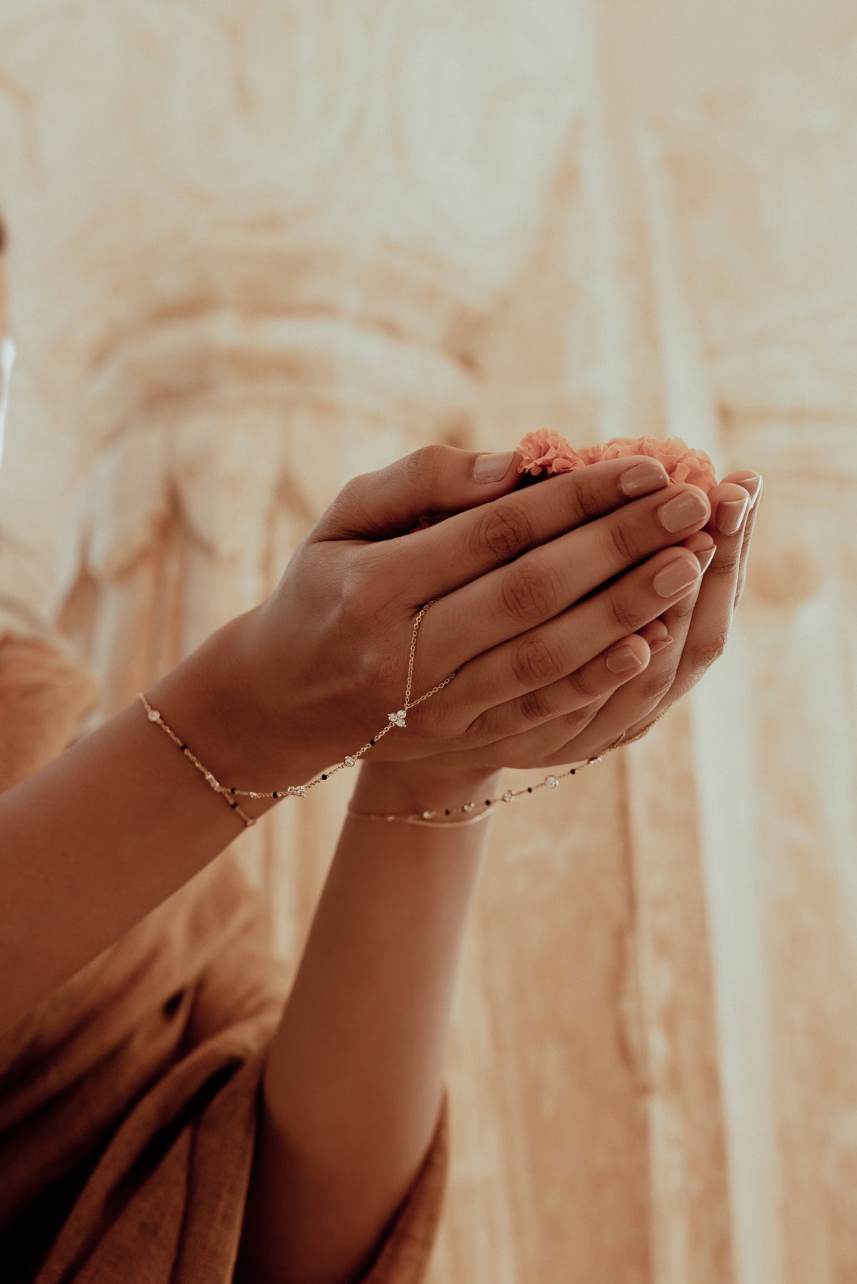 Cupped hands holding marigold petals, a diamond hand chain at the wrist