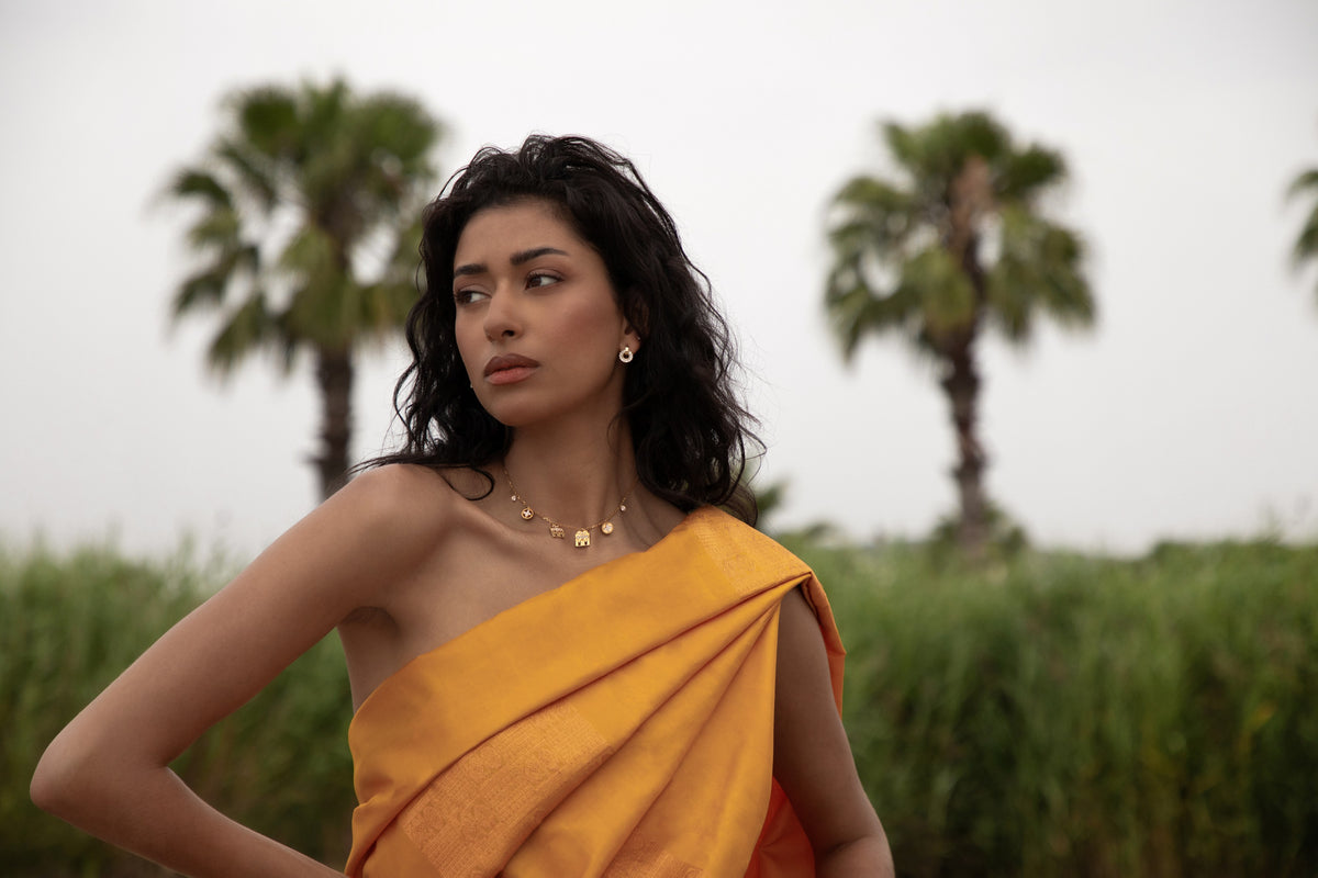 A woman in a mustard silk sari wearing a gold thaali, palms behind her