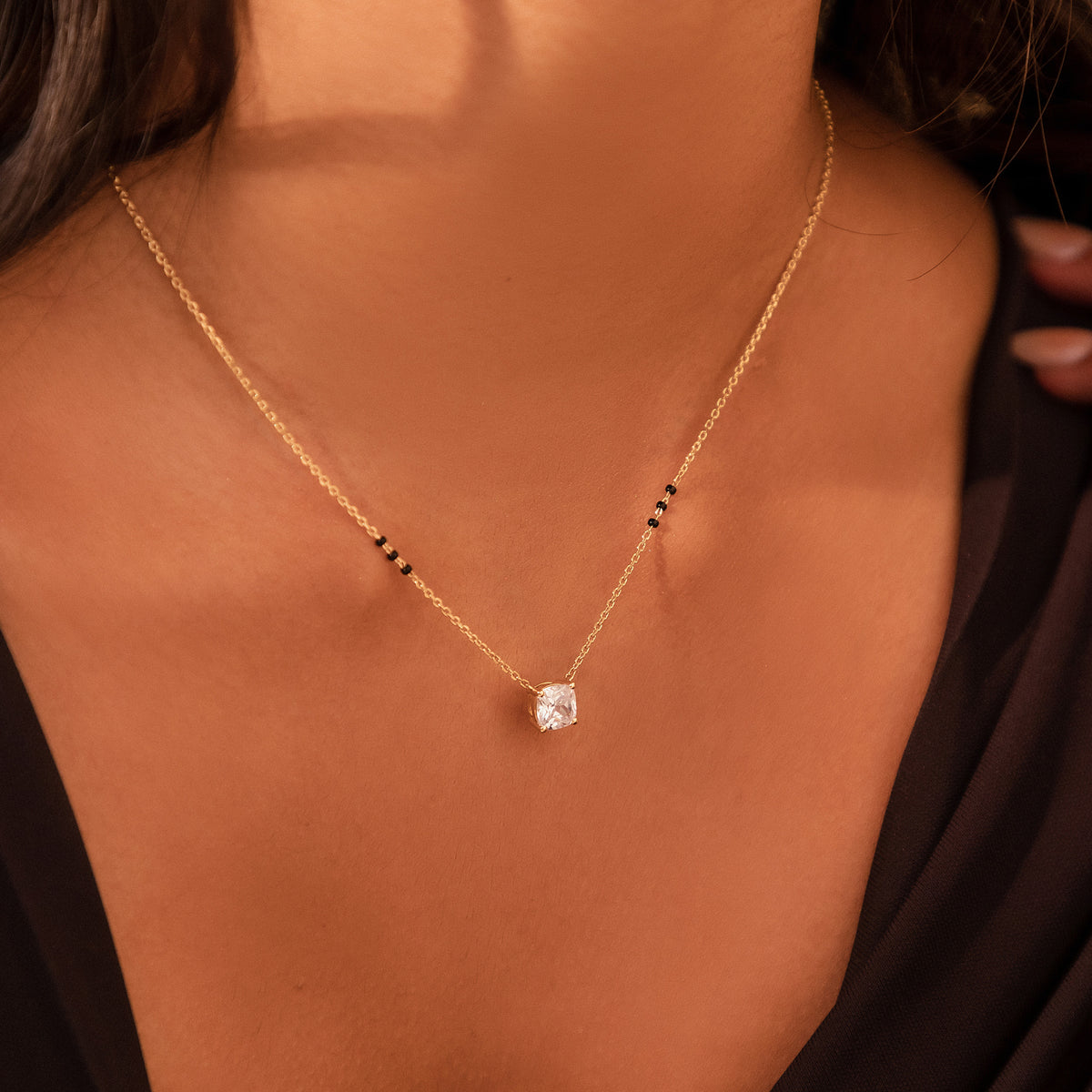 Close-up of the Isha Mangalsutra on a model's neckline in 18K yellow gold, with a cushion-cut lab-grown diamond and three black beads on each side