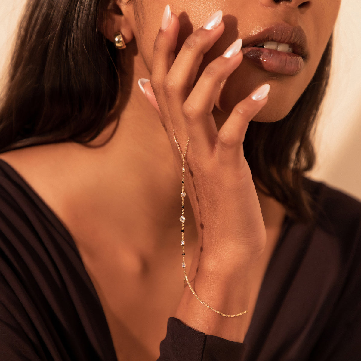 Close-up of a model's hand at her lips wearing the Kanya Handchain Mangalsutra in 18K yellow gold with bezel-set lab-grown diamonds and black beads