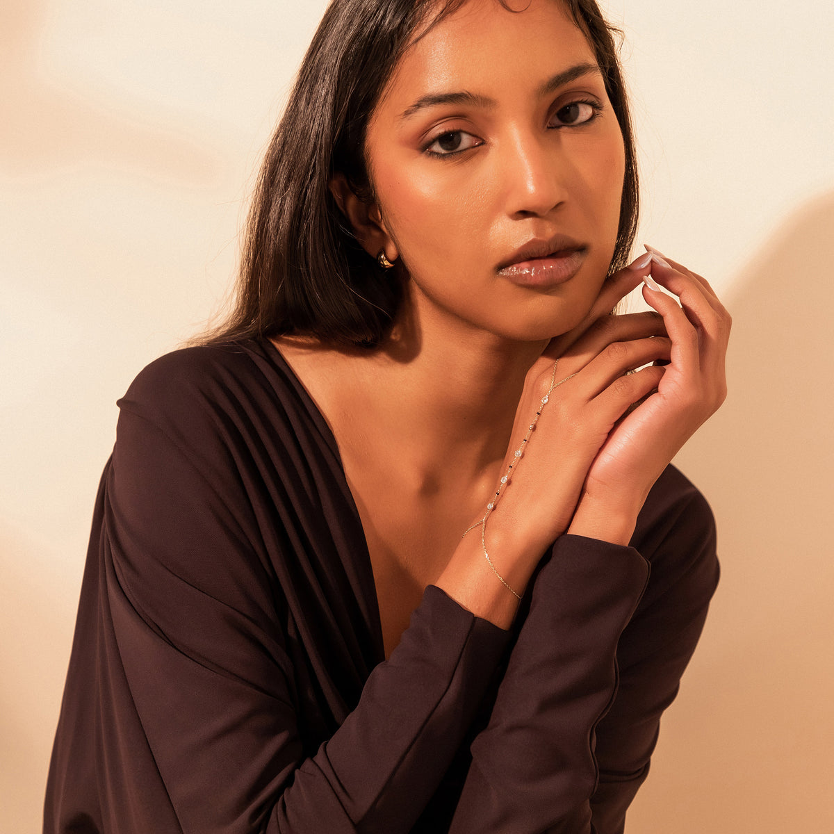 Model facing the camera with hands clasped under her chin, wearing the Kanya Handchain Mangalsutra in 18K yellow gold with bezel-set lab-grown diamonds