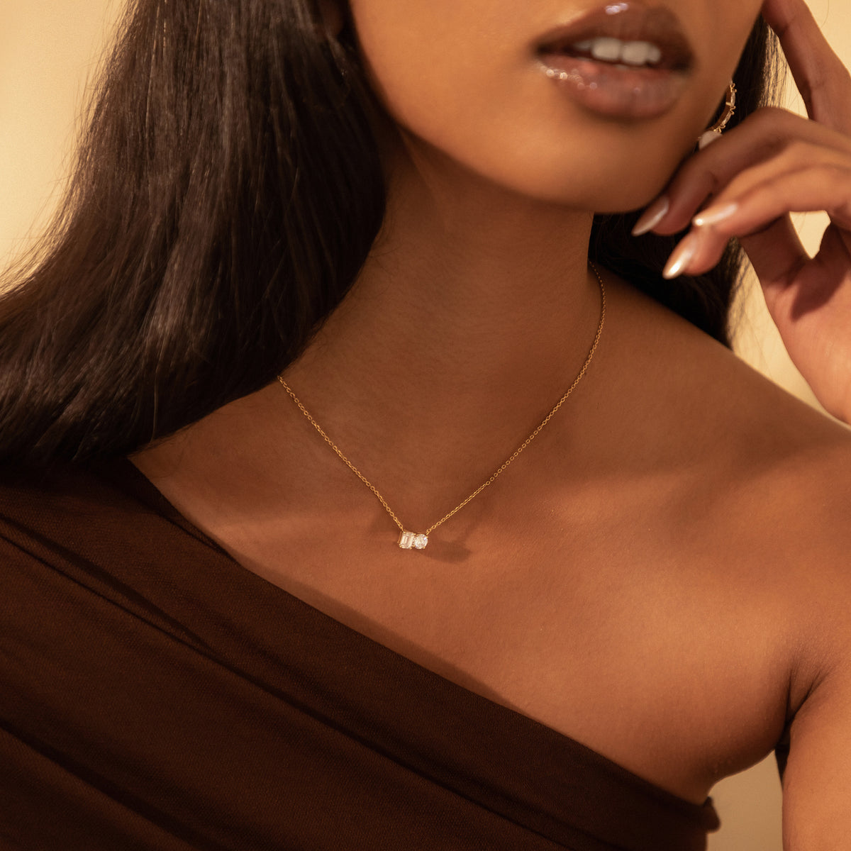 Close-up of the Kira Necklace in 18K gold on a model, with an emerald-cut and a round diamond set side by side