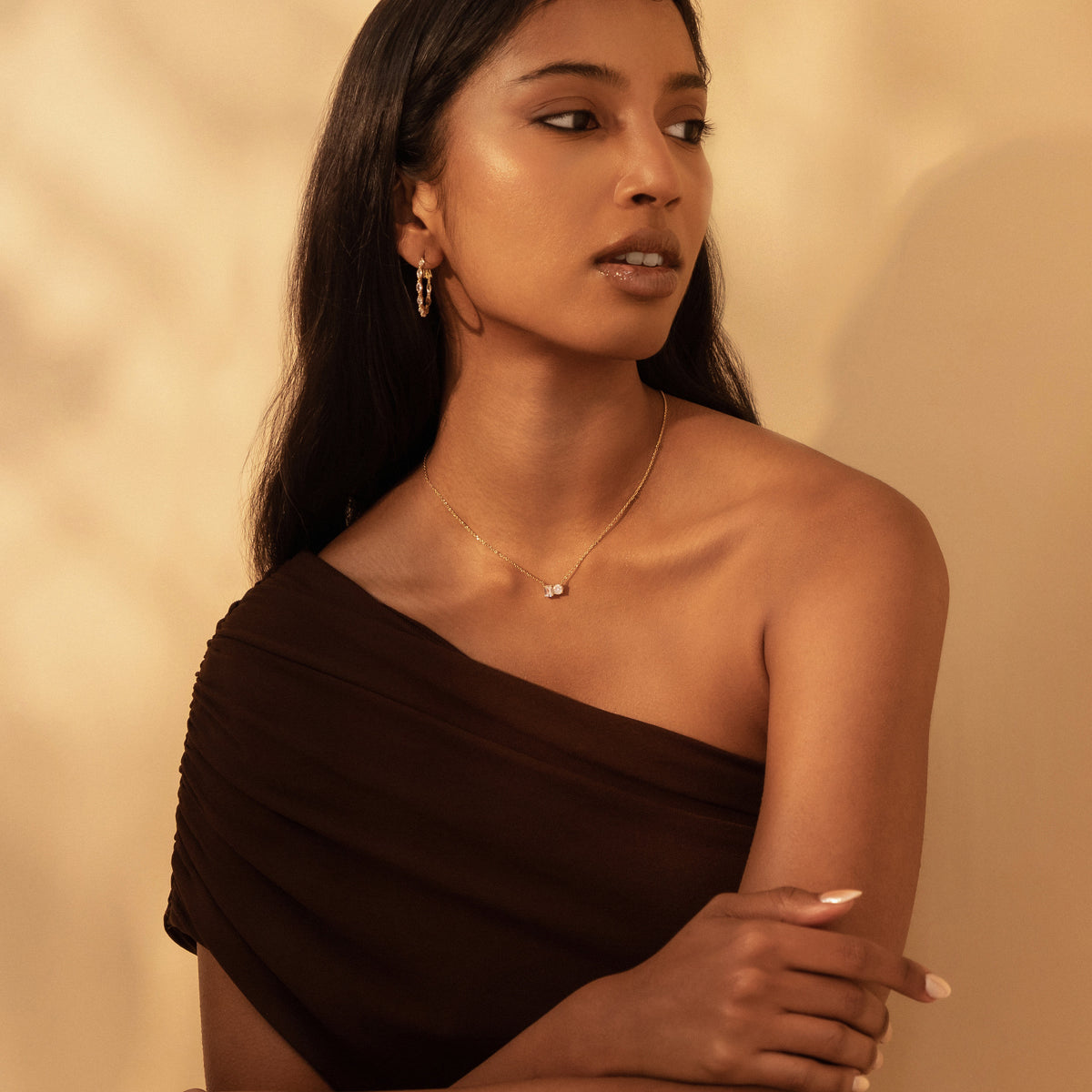Model wearing the Kira Necklace in 18K gold with an emerald-cut and a round diamond, in a one-shoulder top