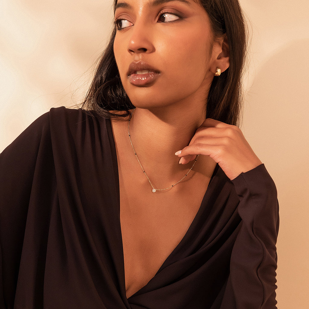 Angled view of model wearing the Modern Mangal Minnie Mangalsutra, showcasing a petite round bezel-set diamond pendant centered on a fine chain with spaced black beads.