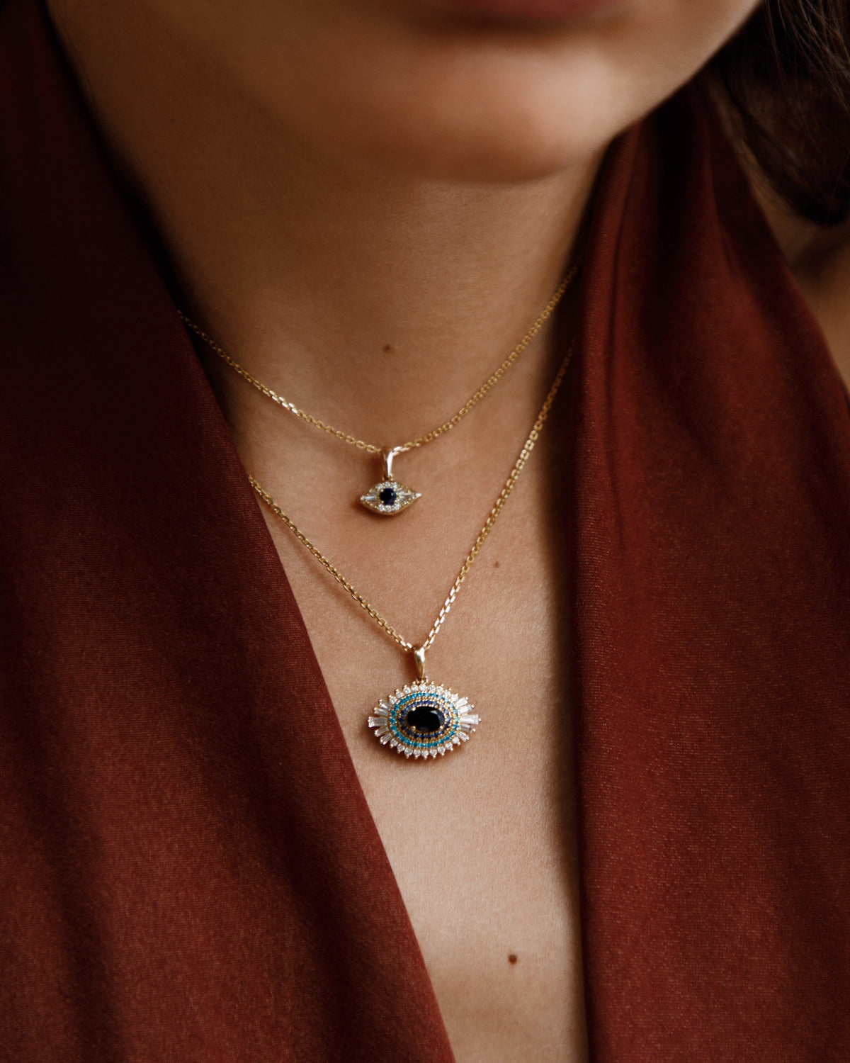 Two evil eye necklaces in gold with black onyx and diamonds, worn layered against a rust top