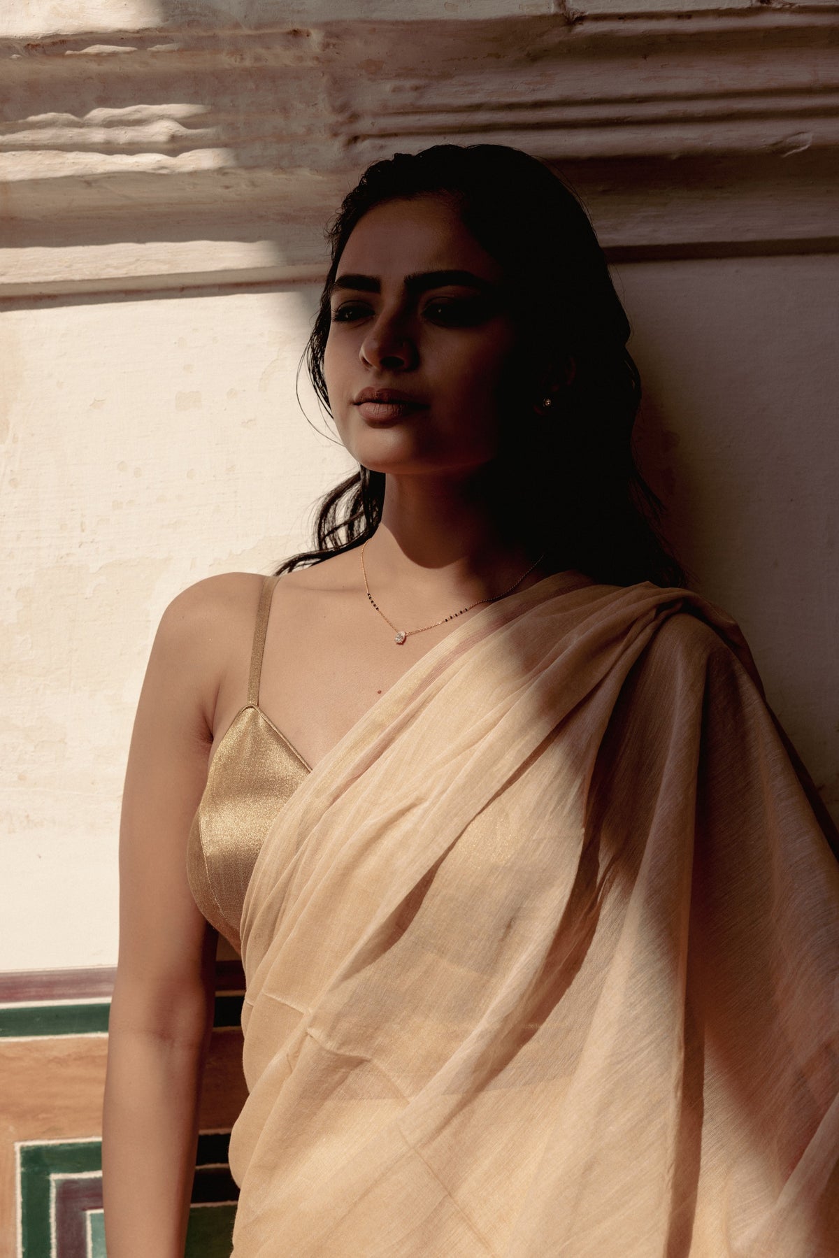Woman in a champagne silk saree wearing a fine diamond mangalsutra against a palace wall in Jaipur