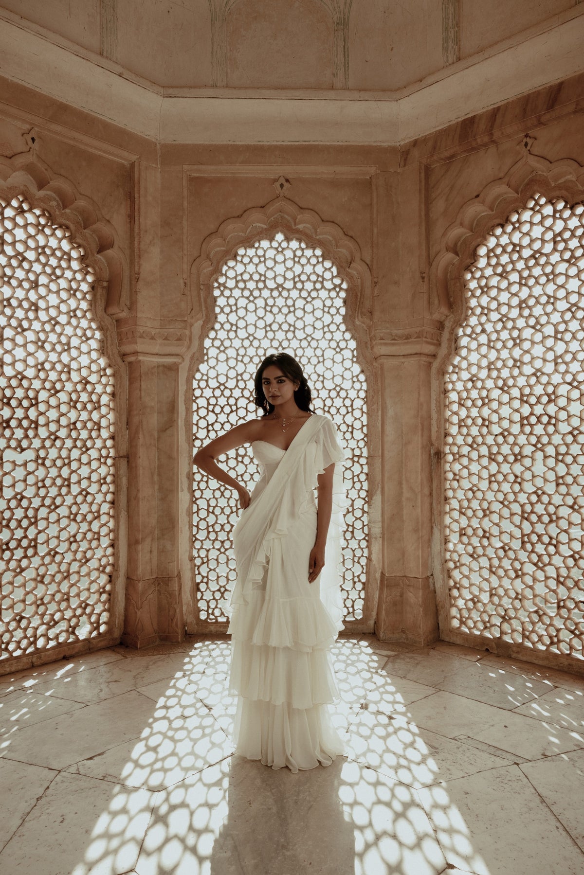Woman in an ivory ruffled saree between carved jaali screens in a Jaipur palace, wearing a Modern Mangal mangalsutra