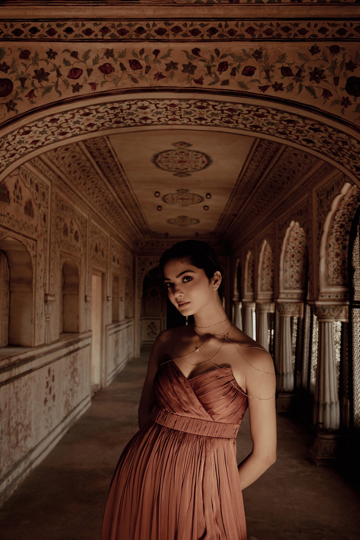 Woman in a blush gown wearing a Modern Mangal mangalsutra in a painted, arched palace corridor in Jaipur