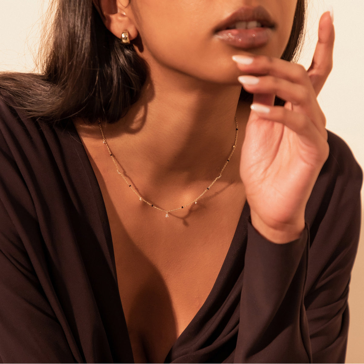 Model wearing the Tara Mangalsutra in 18K yellow gold with scattered lab-grown diamonds and black beads, fingertips at her chin