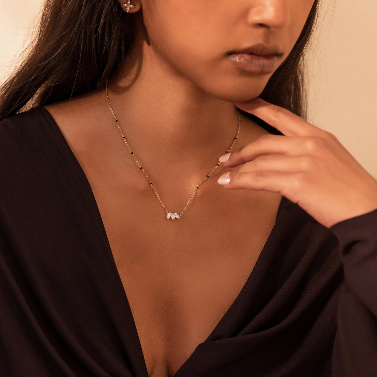 Close-up of a model with fingertips under her jaw wearing the Vanisha Mangalsutra in 18K yellow gold with a marquise lab-grown diamond leaf pendant and black beads